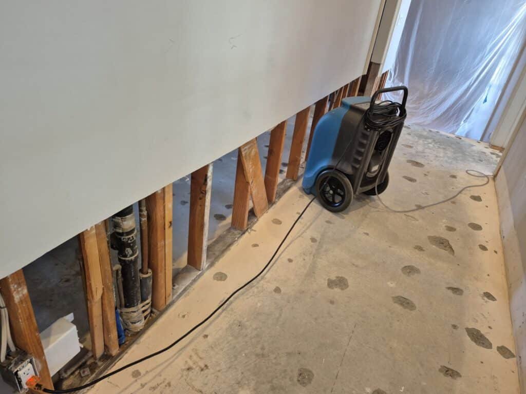 Dehumidifier beside an opened lower wall and exposed framing