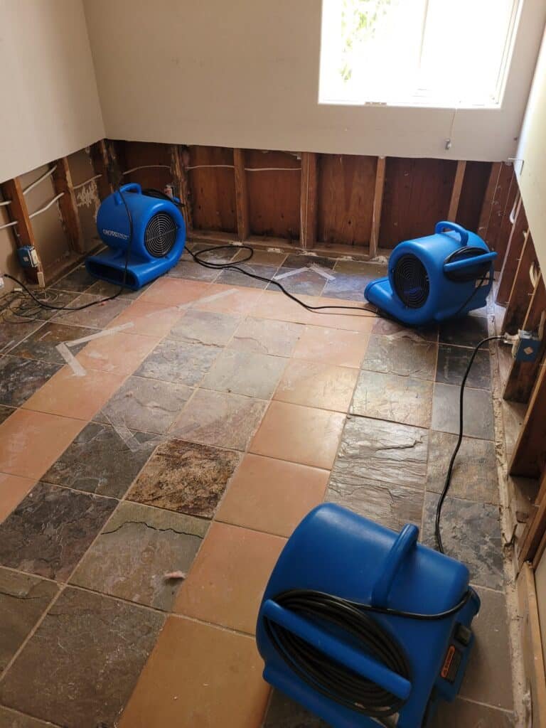 Air movers on a tile floor beside lower walls removed to the framing — Newbury Park