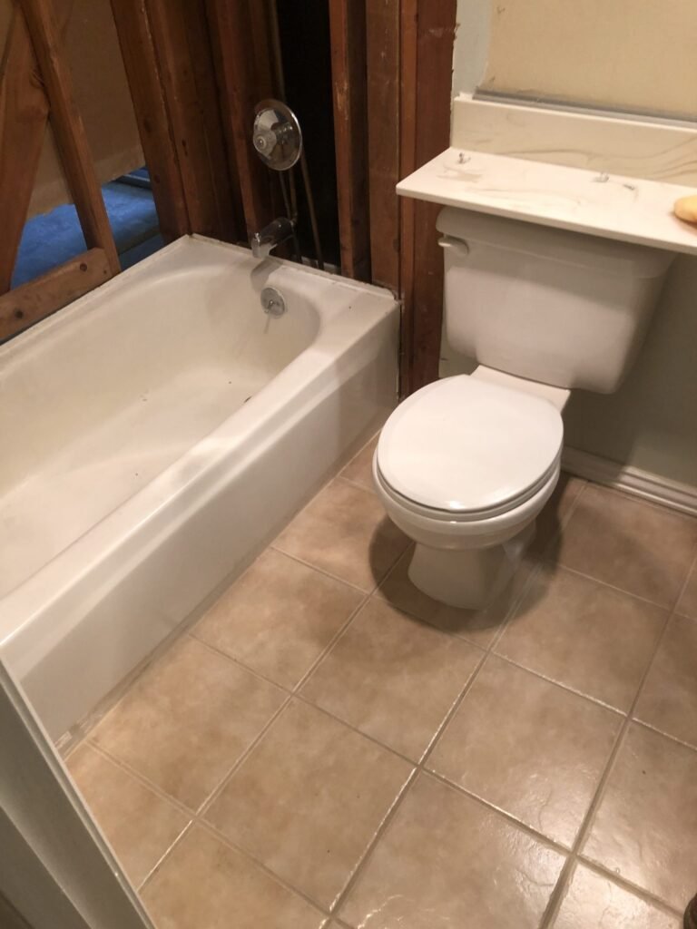 Wall framing exposed beside a bathtub and toilet