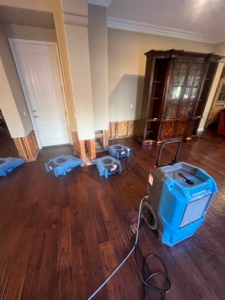 Air movers and a dehumidifier beside opened lower wall sections