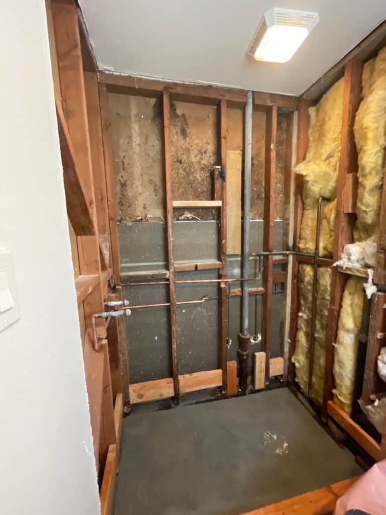 Bathroom wall opened to expose framing and pipes