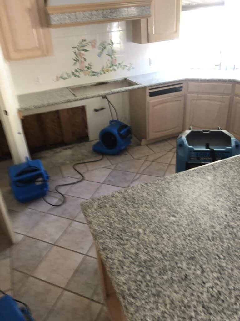 Air movers on a kitchen floor beside opened wall and cabinet areas