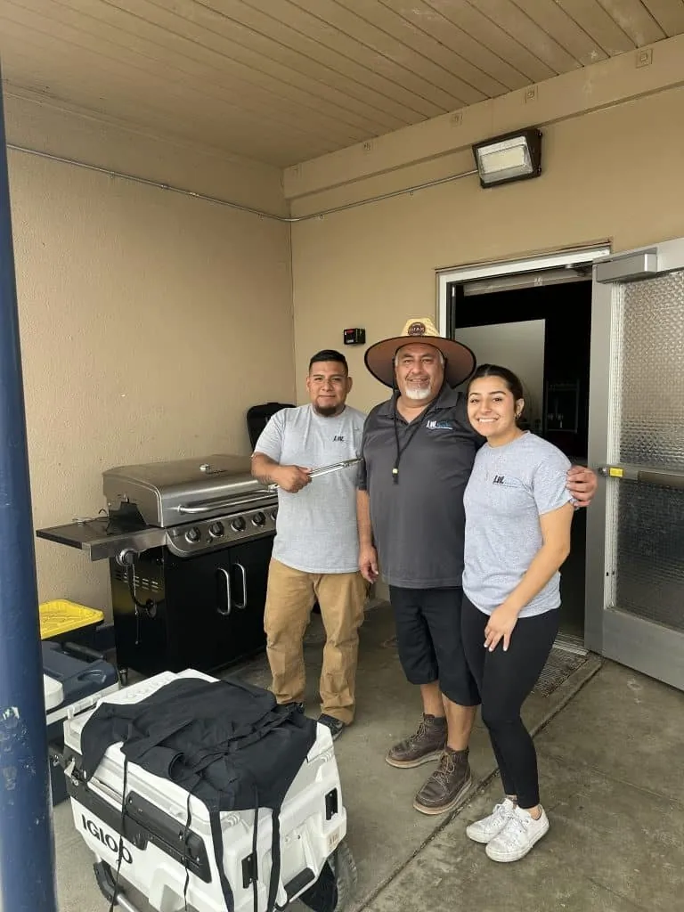 Three people standing beside a barbecue grill